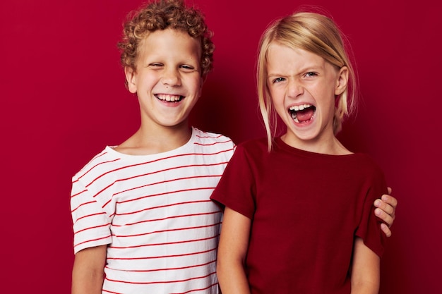 Las emociones lindas de los niños en edad preescolar están una al lado de la otra en ropa de todos los días con fondo rojo