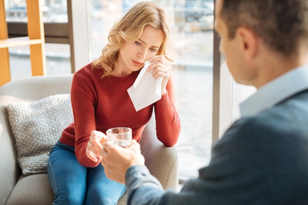 Emociones negativas. Infeliz triste triste mujer sosteniendo un pañuelo de papel y secándose las lágrimas mientras sufre de depresión