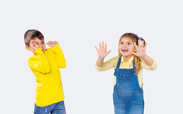 Emociones de los niños. La niña asusta a su amiga haciendo muecas diferentes. Foto sobre fondo blanco.