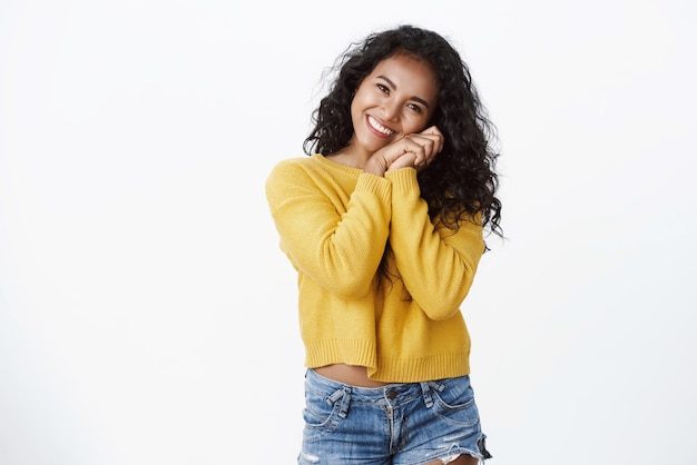 Emoções de felicidade e conceito de pessoas Atraente linda mulher africana de cabelos encaracolados em suéter amarelo incline a cabeça e toque a bochecha suspirando bobo veja cena fofa e macia de fundo branco