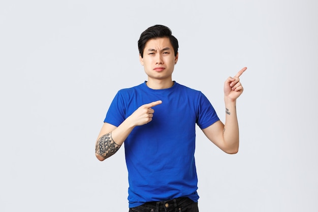 Emoções diferentes, estilo de vida de pessoas e conceito de publicidade. homem asiático descontente e triste de camiseta azul, apontando o dedo para a direita, soluçando e choramingando, reclamando de ciúme e situação incômoda