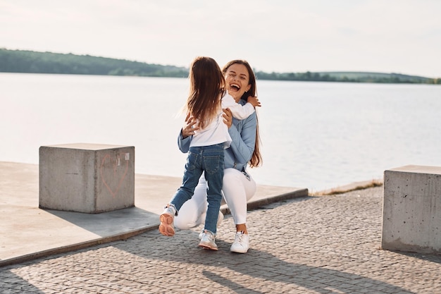 Emoções positivas Jovem mãe com sua filha se divertindo ao ar livre perto do lago no verão