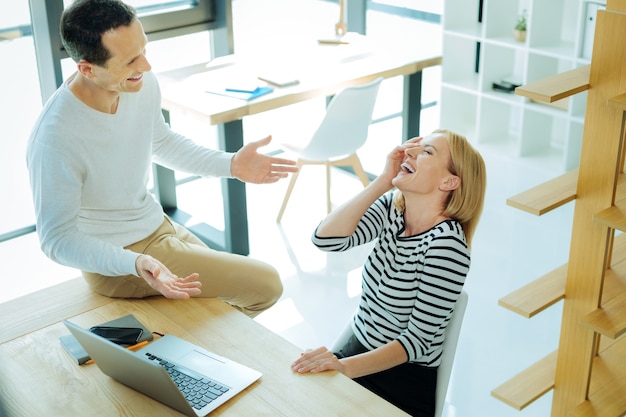 Emoções positivas. Mulher bonita alegre e positiva olhando para seu colega e rindo enquanto ouve suas piadas