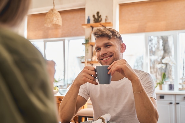 Emoções sinceras. Homem bonito expressando positividade enquanto passa a manhã na cozinha, bebendo chá