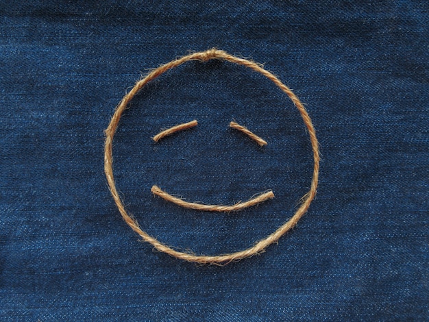 Emoji. Emoticon sonriente hecho de hilo en mezclilla azul. De cerca