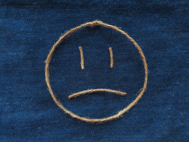 Emoji. Smiley triste hecho de hilo en mezclilla azul. De cerca