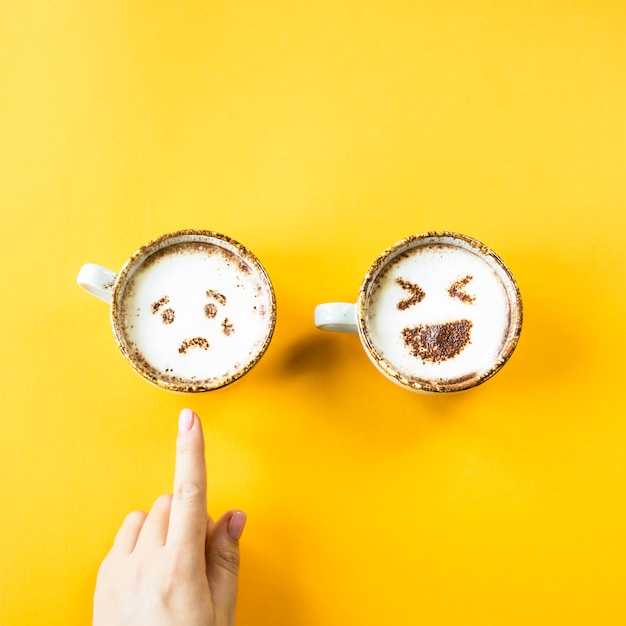 Emojis Gelächter und Traurigkeit werden auf Cappuccinotassen auf gelbem Grund gezeichnet