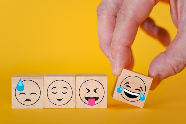 Emoticons Emoji em um fundo amarelo a mão pega um cubo com um emoji sorridente