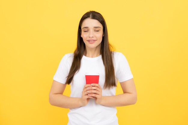 Emotion der jungen schönen Frau trinken heißen Kaffee Schönheit Gesicht natürliches Make-up isoliert auf gelbem Hintergrund