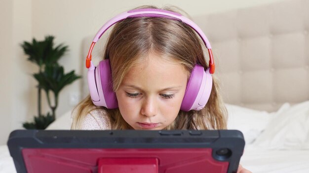 Foto emotional aufgeregtes überraschungskind mit kopfhörern, das zu hause auf dem bett einen digitalen tablet-computer spielt.