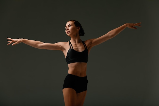 Emotionale Balletttänzerin im Ganzkörperanzug und posiert im Tanz in verschiedenen Posen vor grauem Hintergrund