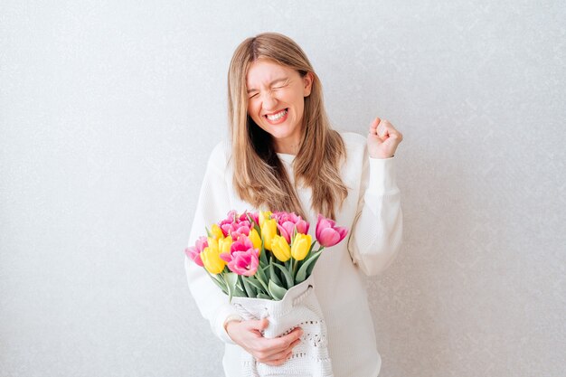 Emotionale Frau, die Tulpen auf weißem Hintergrund hält.