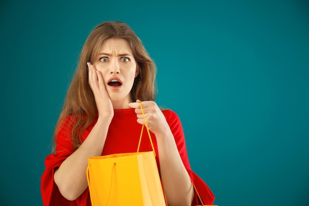 Emotionale junge Frau mit Einkaufstasche auf farbigem Hintergrund