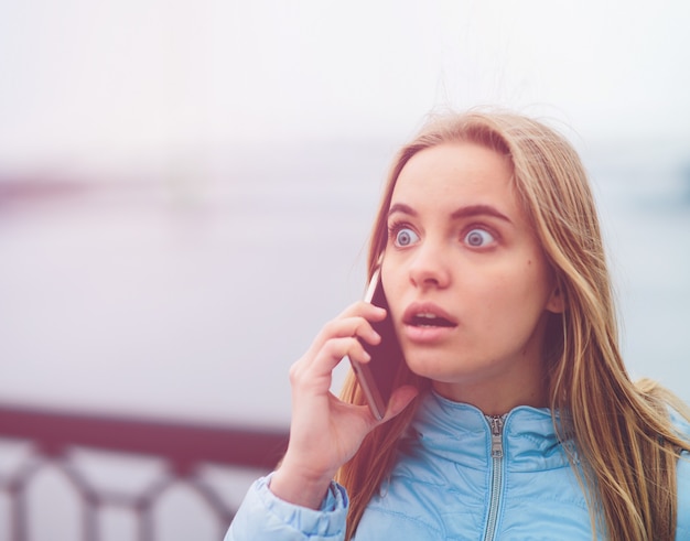 Emotionale schöne Blondine, die draußen am Telefon spricht