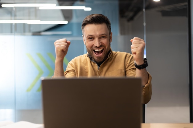 Emotionaler Geschäftsmann, der am Arbeitsplatz mit dem Laptop die Fäuste schüttelt