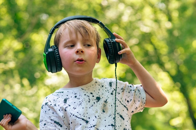 Emotionaler Junge 9 Jahre alt im Wald mit Kopfhörern, die Musik hören