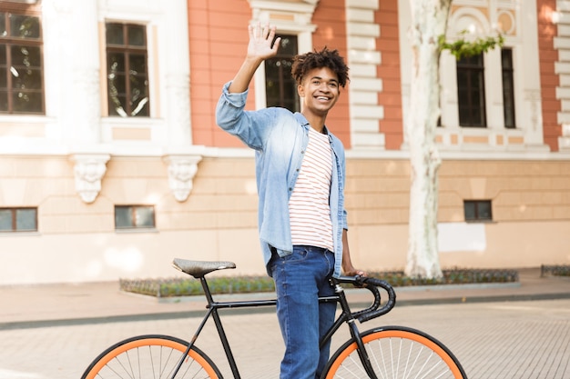 Emotionaler junger Mann auf der Straße im Freien, der mit Fahrrad geht