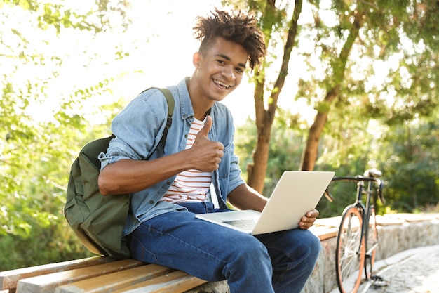 Emotionaler junger Mann im Park im Freien unter Verwendung des Laptops