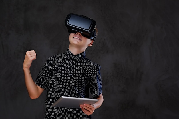 Emotionaler kleiner Junge mit vr-Brille und Tablet-PC. Isoliert auf grauem Hintergrund.