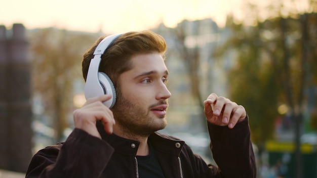 Emotionaler Mann hört draußen über Kopfhörer Musik. Aufgeregter Typ singt beim Spaziergang