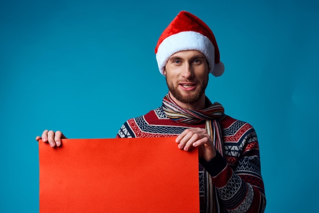 Emotionaler Mann in einer Weihnachtsmütze, der einen blauen Hintergrund des Fahnenurlaubs hält