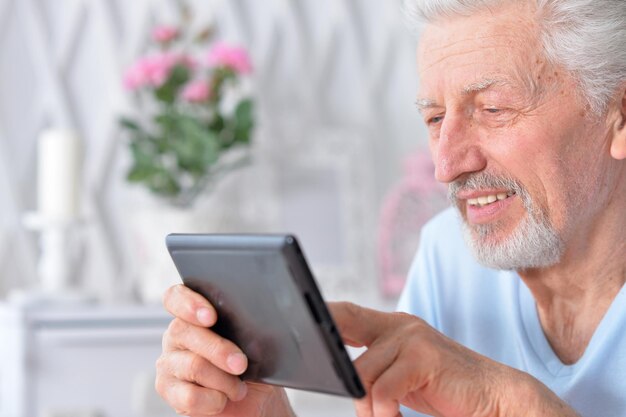 Foto emotionaler schöner älterer mann, der zu hause tablet verwendet