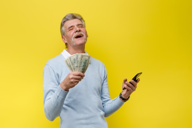 Emotionaler und glücklicher älterer Mann mit Bargeld auf gelber Wand