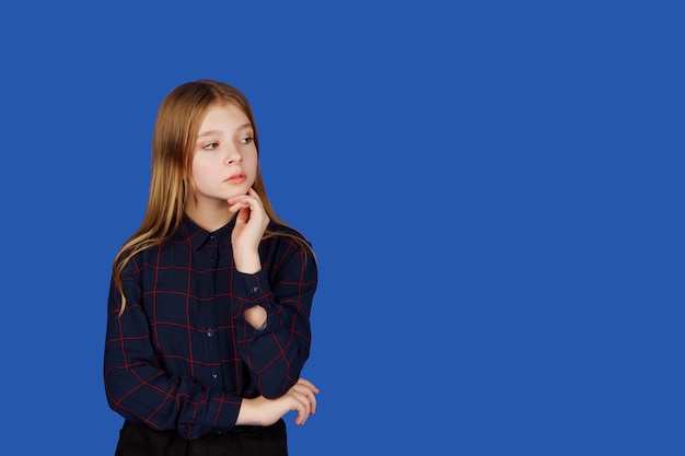 Emotionales dreizehnjähriges süßes Teenager-Mädchen, das denkt und wegschaut, isoliert vor blauem königlichem Hintergrund. Kaukasisches Kind in schwarzer Kleidung zeigt Fragezeichengefühle. Platz kopieren