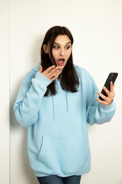 Foto emotionales mädchen mit telefon in blauer jacke auf hellem hintergrund das model ist schockiert