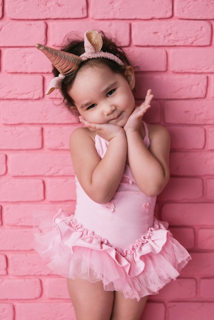 emotionales porträt eines kleinen asiatischen mädchens in einem ballerinakostüm auf rosa hintergrund