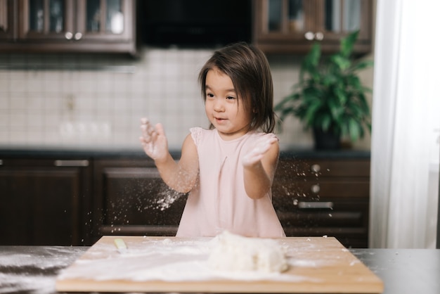 Emotionales schönes kleines Mädchen klatscht in die Hände mit Mehl