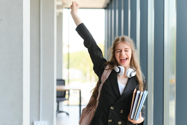 Foto emotionales studentenmädchen innerhalb der wände des instituts feiert eine erfolgreiche prüfung bestehen der highschool oder college zulassung europäischer angestellter erhob die hände fühlt sich glücklich durch gehaltswachstum wurde befördert konzept