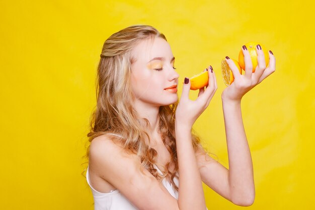 Emotionen, Gesundheit, Menschen, Essen und Schönheitskonzept - Beauty Model Girl nimmt Juicy Oranges. Schönes fröhliches jugendlich Mädchen mit Sommersprossen, lustige Frisur. gelbes Make-up. Professionelles Make-up. Orangenscheibe