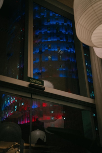 Emotiva fotografía nocturna de un edificio iluminado en azul y rojo visto desde otro edificio