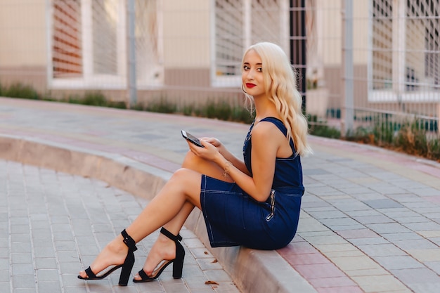 Foto emotive rubia atractiva chica en gafas de sol con teléfono en sol de verano urbano