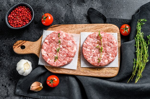 Empanada de pollo crudo, chuletas de carne picada en una tabla de cortar. Carne picada orgánica. Fondo negro. Vista superior