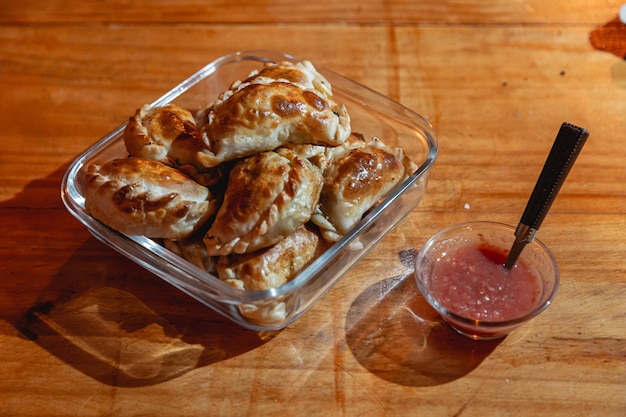 Empanadas al horno sobre una mesa de madera con salsa picante