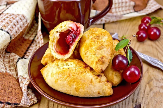 Empanadas de arena con cerezas en un plato, taza, servilleta sobre un fondo de tablas de madera