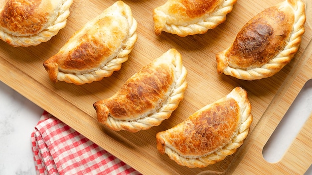 Foto empanadas de carne argentina en una tabla de madera sobre un fondo de mármol y una servilleta roja y blanca