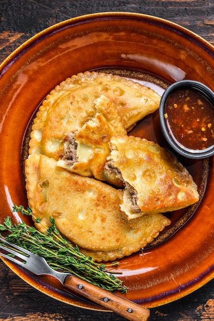 Empanadas fritas con carne de res picada servidas en un plato con salsa de chile