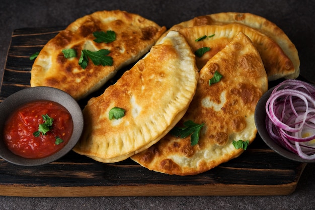 Empanadas fritas caseras con carne de cerdo, chebureks con champiñones sobre una tabla de madera