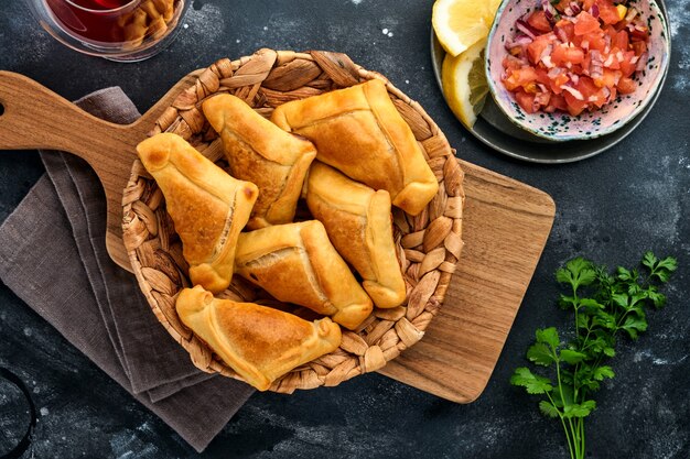 Empanadas fritas con cilantro, carne, huevo, tomate y salsa de ají sobre fondo negro. Plato típico chileno. Concepto de día de la independencia de América Latina y Chile.