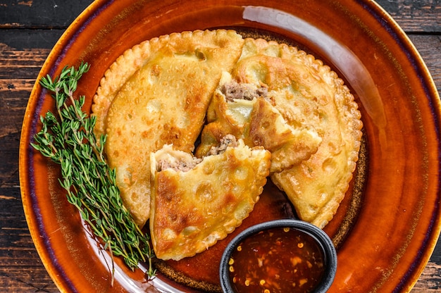 Empanadas fritas com carne picada de carne bovina servidas em prato com molho de pimenta. Fundo de madeira escuro. Vista do topo.