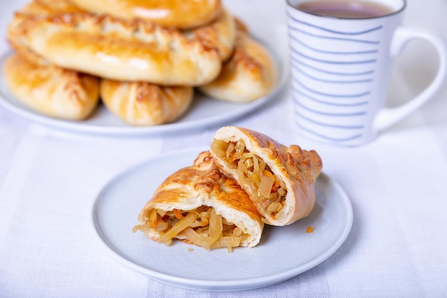 Empanadas (pirozhki) con repollo. Repostería casera. Cocina tradicional rusa y ucraniana. En el fondo hay un plato con empanadas. De cerca.