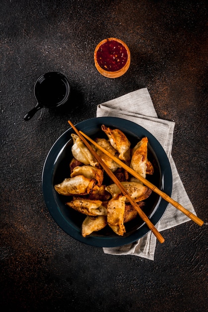 Empanadillas asiáticas fritas Gyoza en plato oscuro servido con palillos y salsa de soja