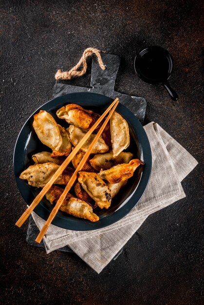 Empanadillas asiáticas fritas Gyoza en plato oscuro servido con palillos y salsa de soja