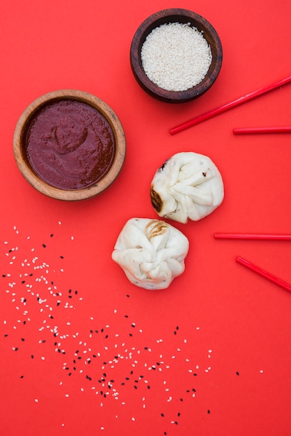 Empanadillas chinas con salsas para la cena con tazón de sésamo y palillos sobre fondo rojo