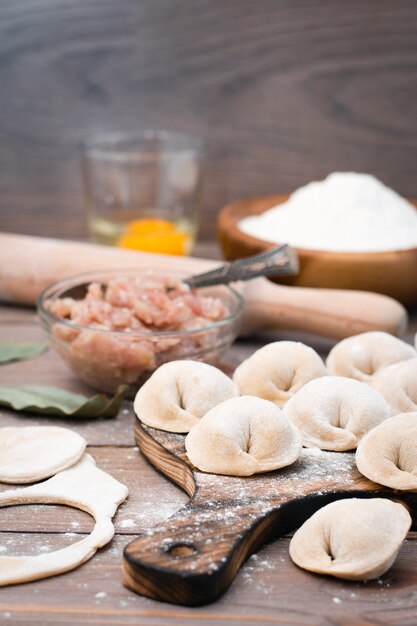 Empanadillas crudas en la tabla de cortar e ingredientes para su preparación: harina, huevo, carne picada en una mesa de madera