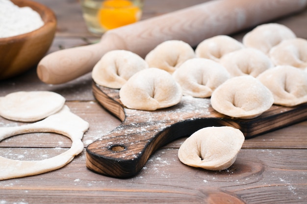 Empanadillas crudas en una tabla de cortar e ingredientes para su preparación en una mesa de madera