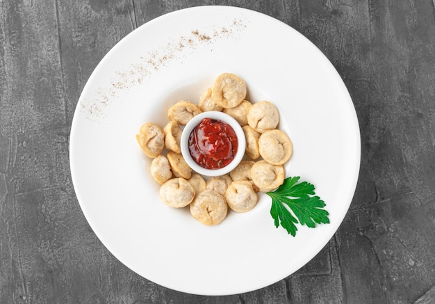 Empanadillas fritas con salsa de tomate. En un plato blanco grande. Decorado con perejil. Vista desde arriba. Fondo de hormigón gris.